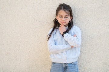 Beautiful girl in red glasses stands near the wall with her arms crossed. Educational children's...