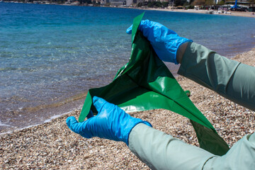 Green garbage bag in hands against the background of the sea and beach