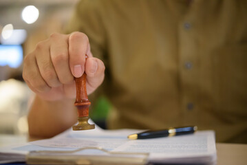 Hand using a rubber stamp on official papers, representing approval process, legal documentation,...