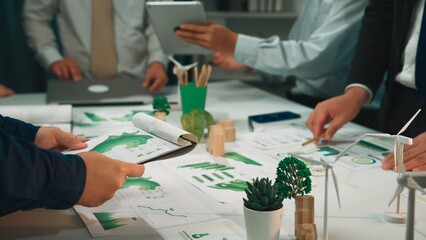 A diverse team engages in a collaborative meeting focused on sustainability strategies, utilizing charts, models, and green elements to discuss eco-friendly business development. SACTR