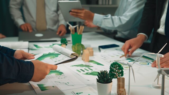 A diverse team engages in a collaborative meeting focused on sustainability strategies, utilizing charts, models, and green elements to discuss eco-friendly business development. SACTR