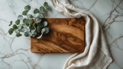 Wood cutting board with a linen napkin and a plant placed on a marble table, viewed from above with blank space.