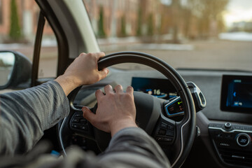 Close-up of a driver's hands pressing the horn while gripping the steering wheel of an electric car. Dashboard displays driving data. Urban road in the background. Road aggression, traffic jam concept
