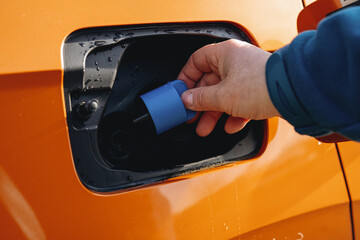 Filling the fuel tank of a vibrant orange vehicle at a gas station on a sunny day in August