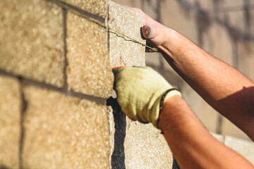 Bricklayer constructs stone wall using cement and tools while wearing gloves