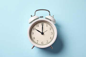 White alarm clock on light blue background, top view