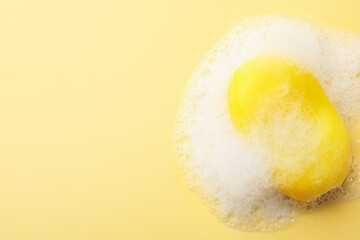 Soap bar with foam on yellow background, top view. Space for text