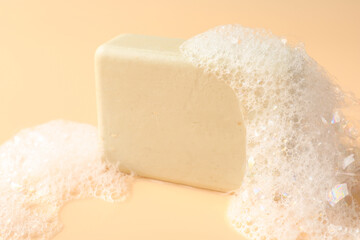Soap bar with foam on beige background, closeup