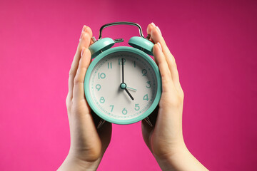 Woman with turquoise alarm clock on bright pink background, closeup