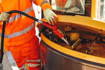 Close-up of mechanic refueling heavy machinery at construction site while wearing safety uniform...