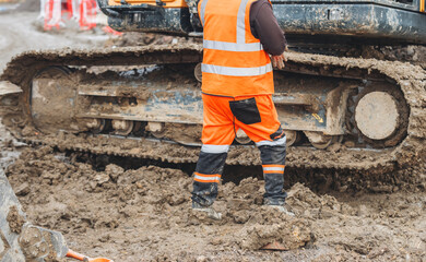 Builder in safety gear operating machinery on muddy site