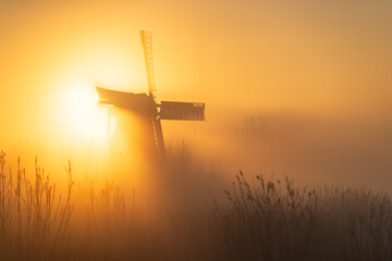 Sunrise at a Dutch, traditional windmill and a canal in the spring fog.