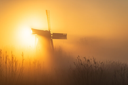 Sunrise at a Dutch, traditional windmill and a canal in the spring fog.