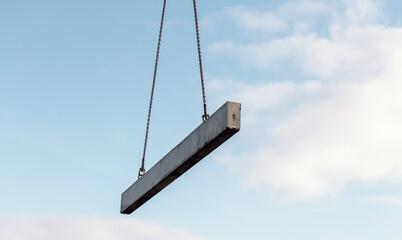 Heavy concrete beam suspended by chains against clear sky during construction work
