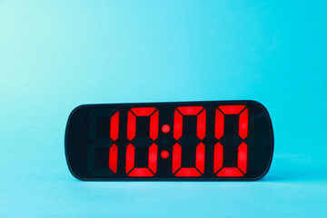 Digital alarm clock showing 10:00 o'clock on light blue background
