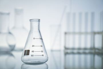 Empty flask on mirror surface against light background, space for text. Laboratory equipment