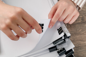 Woman attaching sheets of paper with metal binder clip at table, closeup