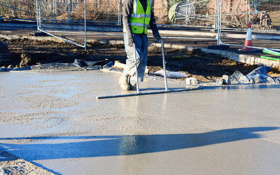 A construction worker uses screeding tool to level freshly poured concrete on  building site