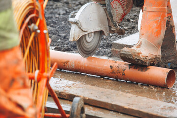 Builder cuts large drainage pipe using  power cutter at construction site