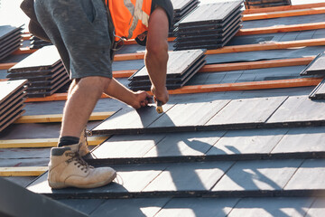 Roofer installs roofing tiles at building site using hand tools to ensure proper alignment and stability on sloped surface
