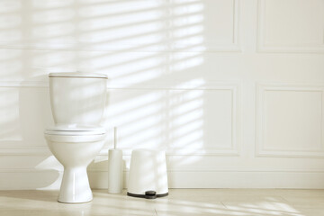 Toilet bowl, trash bin and cleaning brush near white wall indoors. Space for text