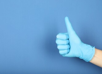 Doctor in medical glove showing thumbs up on blue background, closeup. Space for text