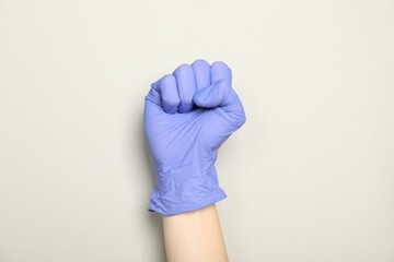 Doctor in medical glove showing fist on light grey background, closeup