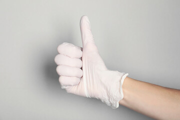 Doctor in medical glove showing thumbs up on light grey background, closeup