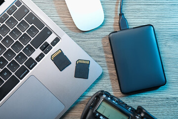 Hard disk drive with USB cable, SD memory cards, camera and laptop on wooden table, flat lay