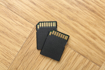 Two SD memory cards on light wooden table, top view