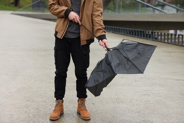 Man with broken umbrella fighting wind under rain outdoors, closeup