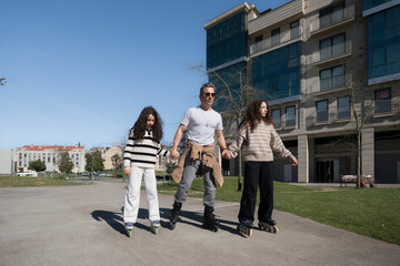 Father skating with daughters in urban park, holding hands and enjoying family time