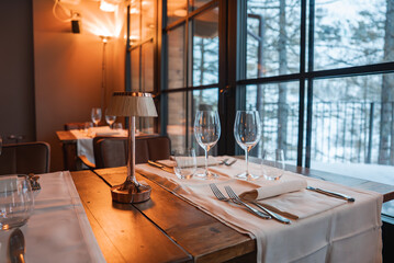 Refined dining table with lamp, napkins, and glassware inside a luxury alpine hotel. Large windows...