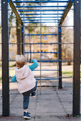 Little girl is climbing the chain ladder in the playground. Back view