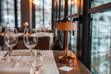 A luxury restaurant dining table with glassware, a white tablecloth, and a copper lamp, set against a snowy landscape in the Italian Alps.
