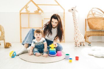 Naklejka premium Cute mom and baby 6-9 months sitting on the floor and playing together indoors at home