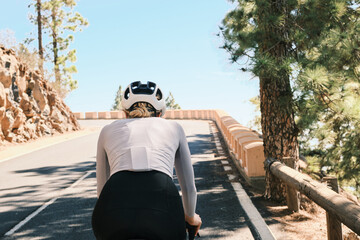Rear view of a female cyclist riding a bike on a scenic mountain road.  She wears a helmet and long sleeve jersey. Perfect for active lifestyle, sports, and travel themes.