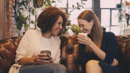 Two friends chatting and sipping coffee in city cafe after a long workday