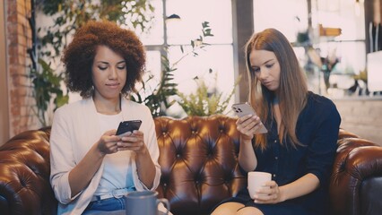 Two friends scrolling on their phones in cafe, disconnected in social setting