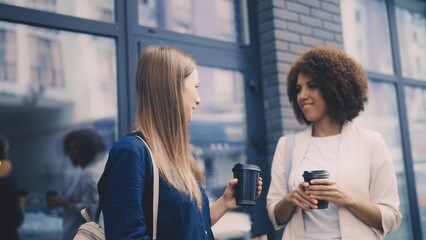 Two pretty women standing outside coffee shop, chatting and enjoying coffee-to-go