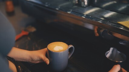 Closeup of barista holding cup of coffee with steamed milk, hot beverage ready to serve