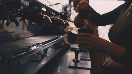 Closeup of female barista pouring steamed milk into coffee, latte preparation process