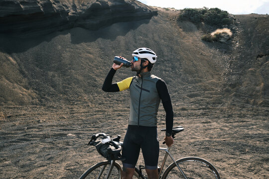 Cyclist takes a break, enjoying a refreshing drink amidst a rugged, volcanic landscape.  Epic adventure and endurance themes. - Powered by Adobe