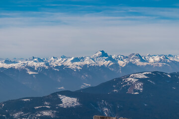 Majestic snow-covered peaks of Julian Alps, featuring Mangart, rise against blue sky with light...
