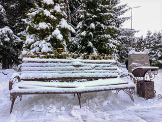 A bench covered in snow next to a tree covered in trees