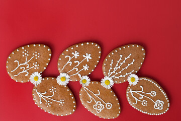 Romantic decorated Easter gingerbread cookies in a shape of egg, with daisy flowers, red background