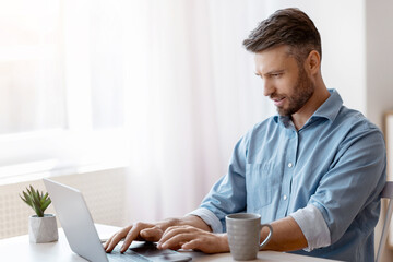 Unemployed man scrolling job search website at home using laptop computer, handsome male freelancer...