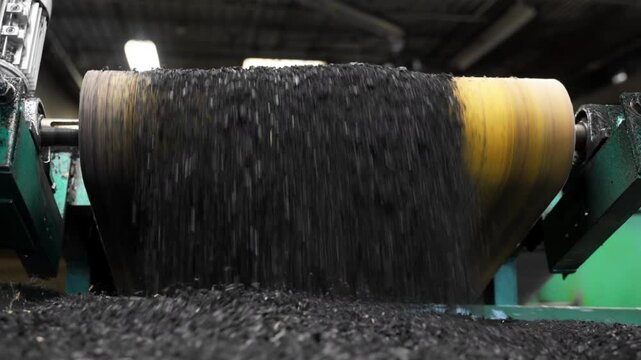 Heavy machinery grinding old rubber tires into small particles for reuse in construction or road surfacing.