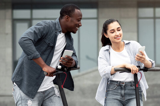 Lifestyle Concept. Cheerful diverse couple using cell phones and riding stand-up scooters, copy space - Powered by Adobe