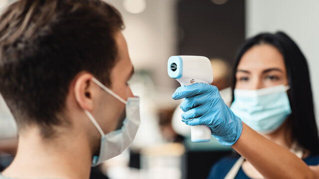 New rules of life. Hairdresser checking body temperature of client at barber shop - Powered by Adobe